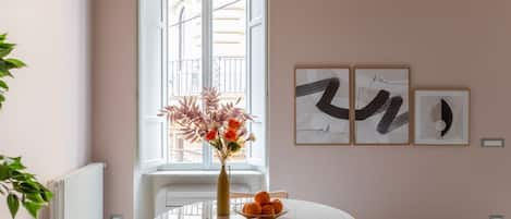 Un comedor con una mesa redonda, sillas, un jarrón con flores y cuadros en la pared.