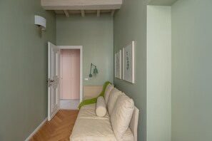 Käytävällä on beige sohva, vihreä huopa ja seinällä on kehystettyjä kasvitieteellisiä kuvia.