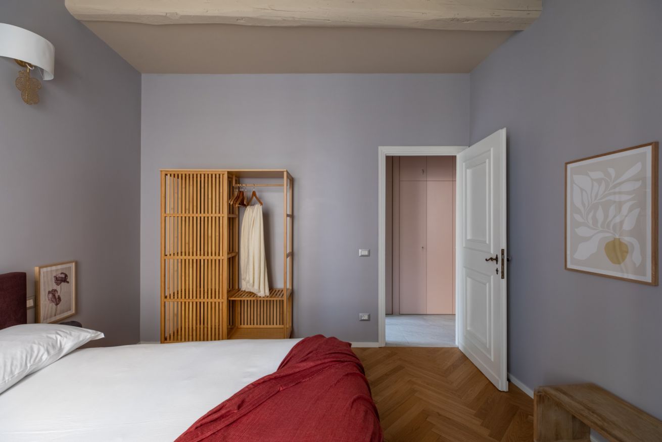 A bedroom with a bed, a wooden wardrobe, a bench, and a door leading to another room.