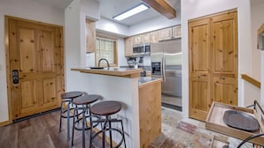 Een moderne keuken met houten kastjes, een roestvrijstalen koelkast en een bar voorzien van krukken.
