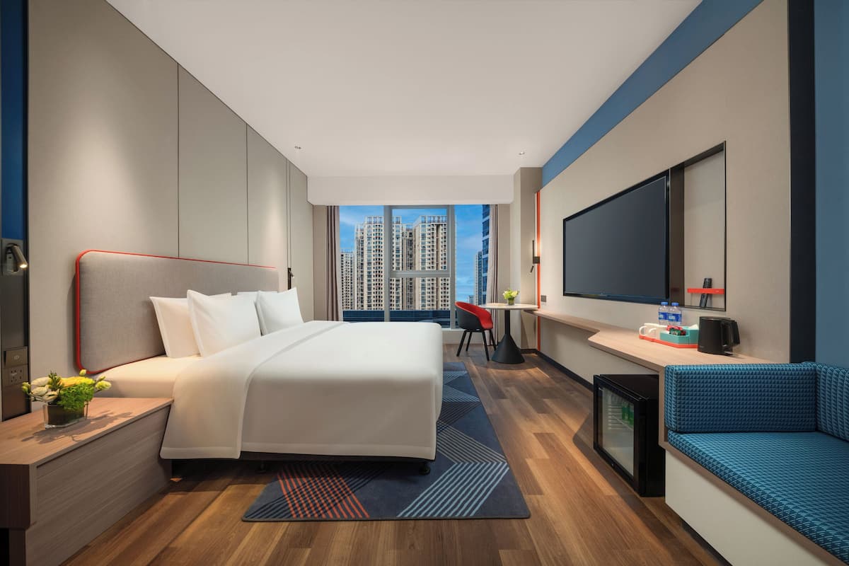 Une chambre d’hôtel moderne dotée d’un grand lit, d’un bureau, d’une télévision et offrant une vue sur les gratte-ciel.