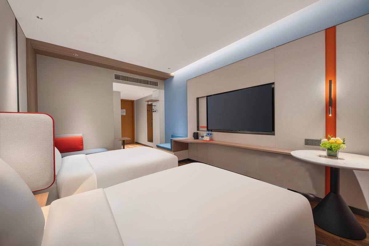 Une chambre d’hôtel moderne avec deux lits, une télévision, une petite table avec un vase et une chaise rouge.