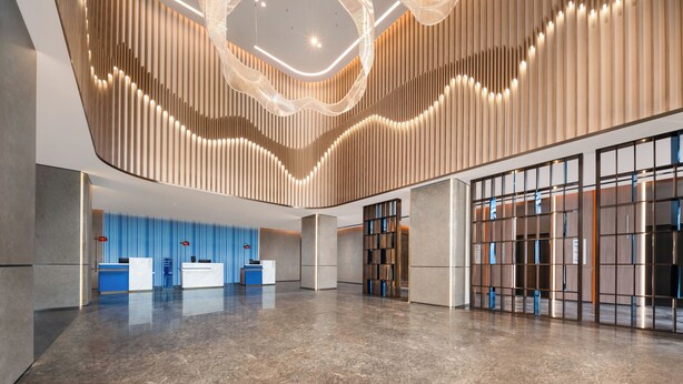 Un hall d’entrée spacieux au design moderne, comprenant un comptoir d’accueil, un mur bleu et un mur en panneaux de bois doté d’un éclairage intégré.