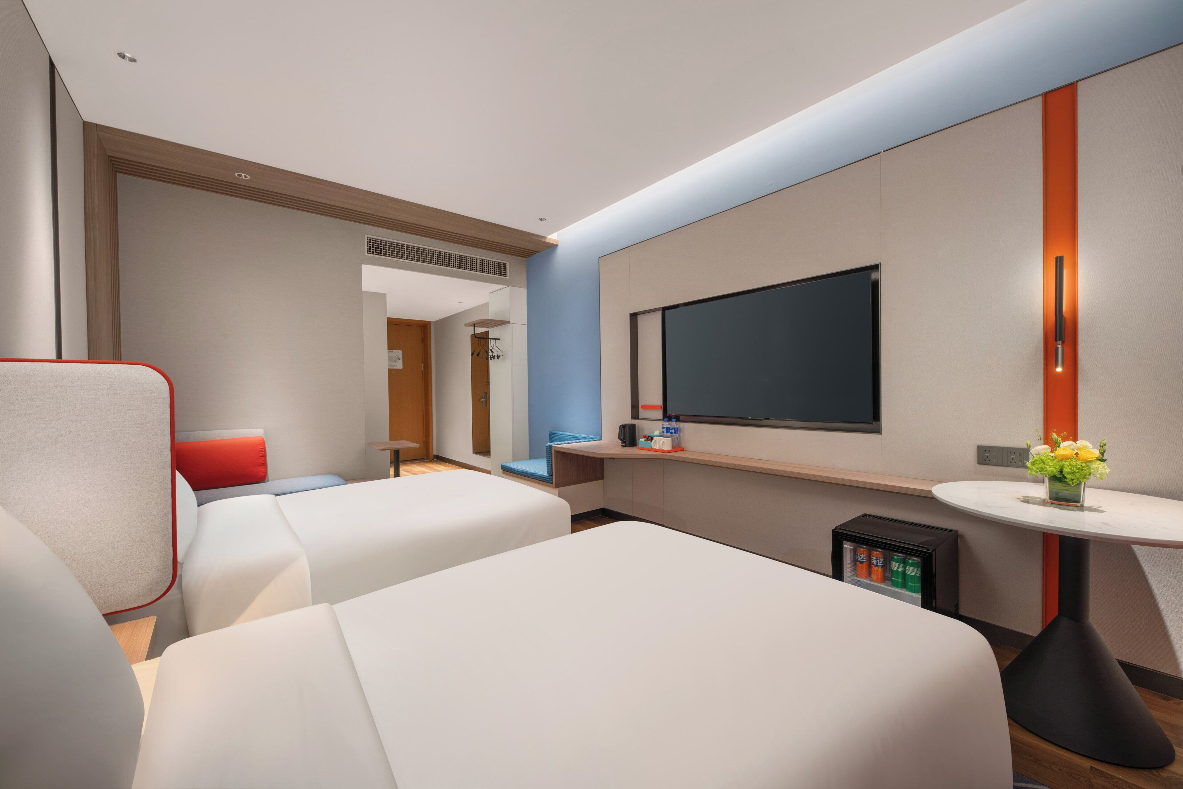 Habitació d'hotel amb dos llits, televisió de pantalla plana, una taula petita amb un vas i un minibar.
