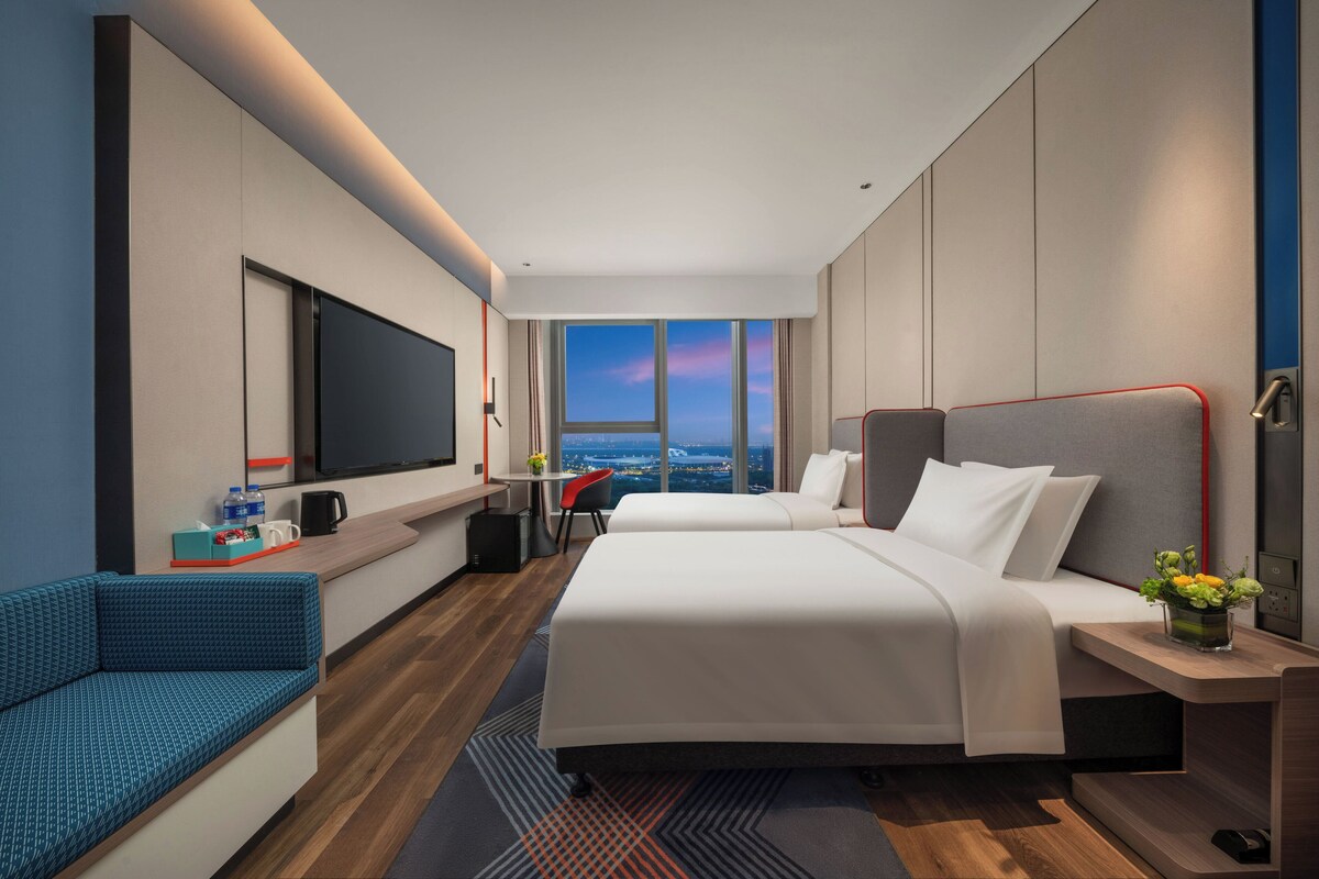 Une chambre d’hôtel moderne avec deux lits, une télévision, un bureau et une vue sur la ville.