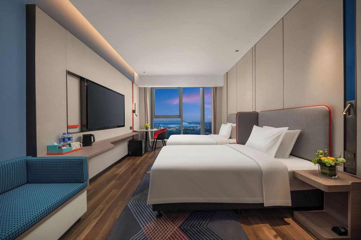 Une chambre d’hôtel moderne avec deux lits, une télévision, un bureau et une vue sur la ville.