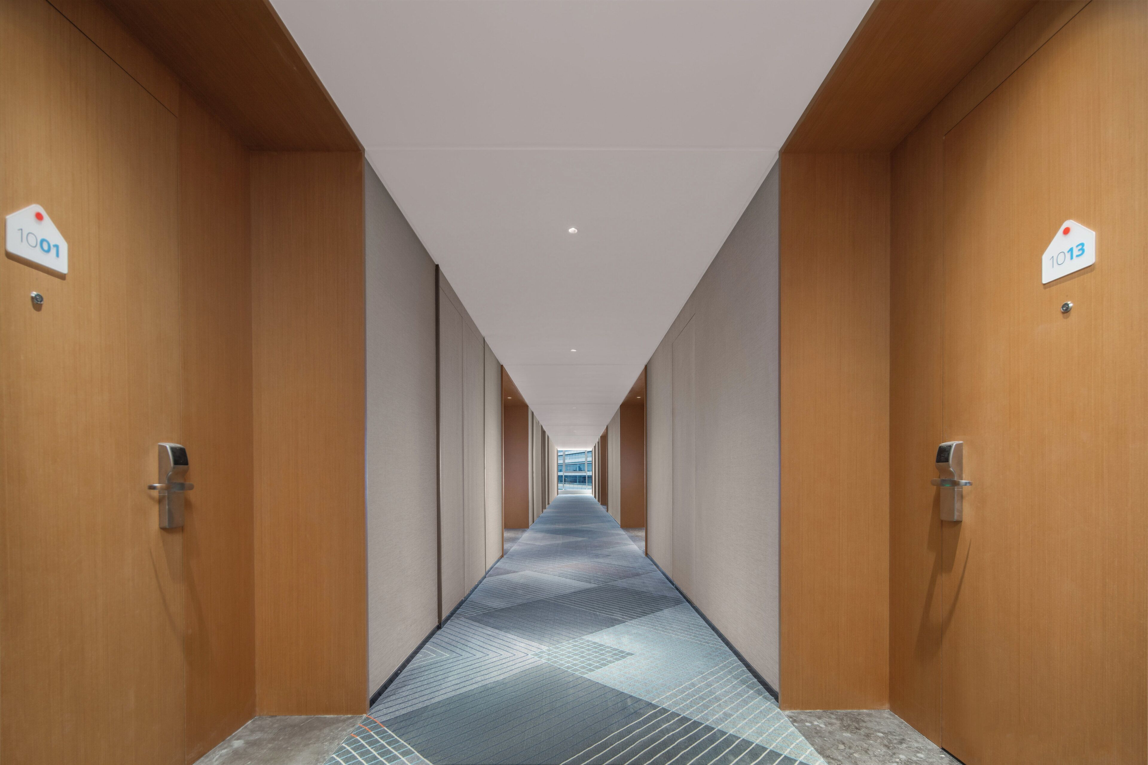 Un pasillo con paredes de madera, puertas numeradas y piso con diseño.