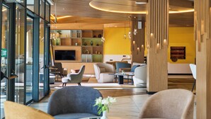 A modern lobby with a wooden ceiling, a large flat-screen TV, and a variety of seating arrangements including sofas and armchairs. - Holiday Inn Tashkent City by IHG (Tashkent)