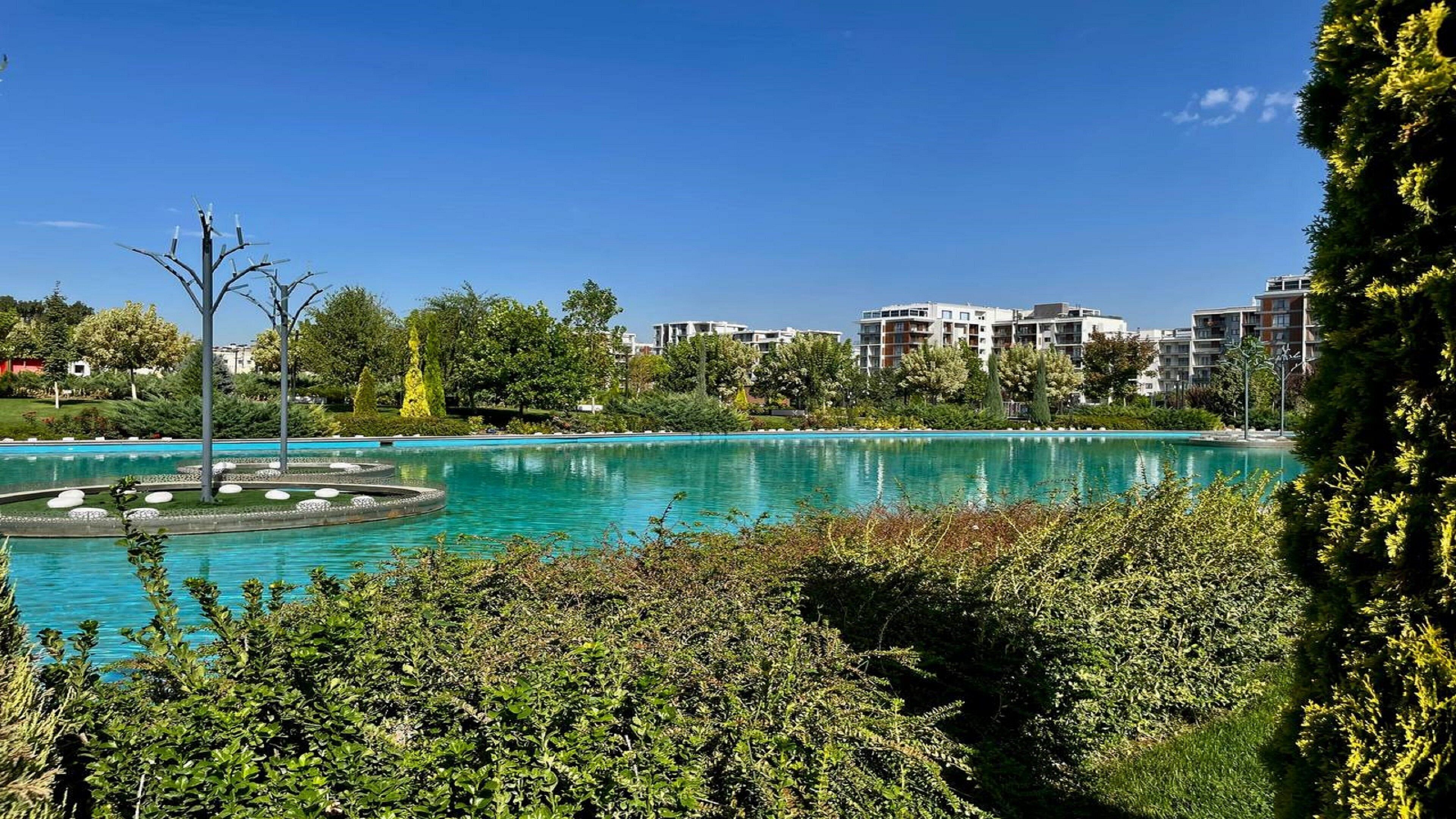 A pool surrounded by greenery and modern buildings in the background.
