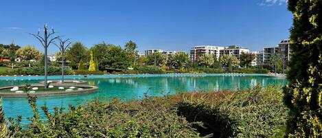 Piscina cercada por vegetação e edifícios modernos ao fundo.