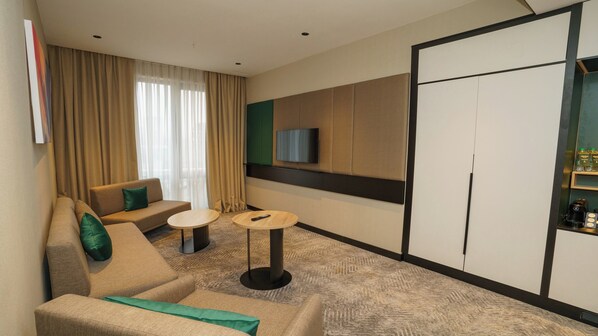 A hotel room with a sofa, two side tables, a television, and a minibar.