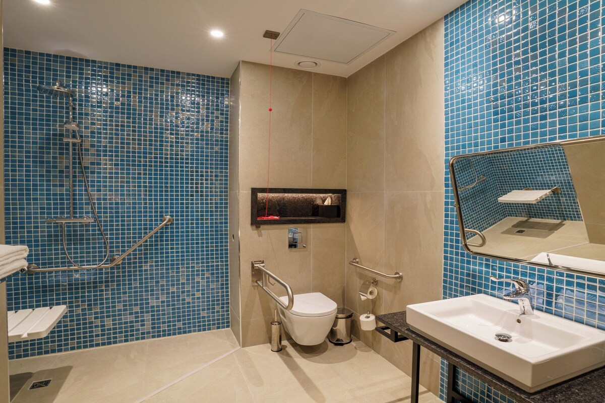 A bathroom with blue mosaic tiles, a white sink, a toilet, and a shower area.