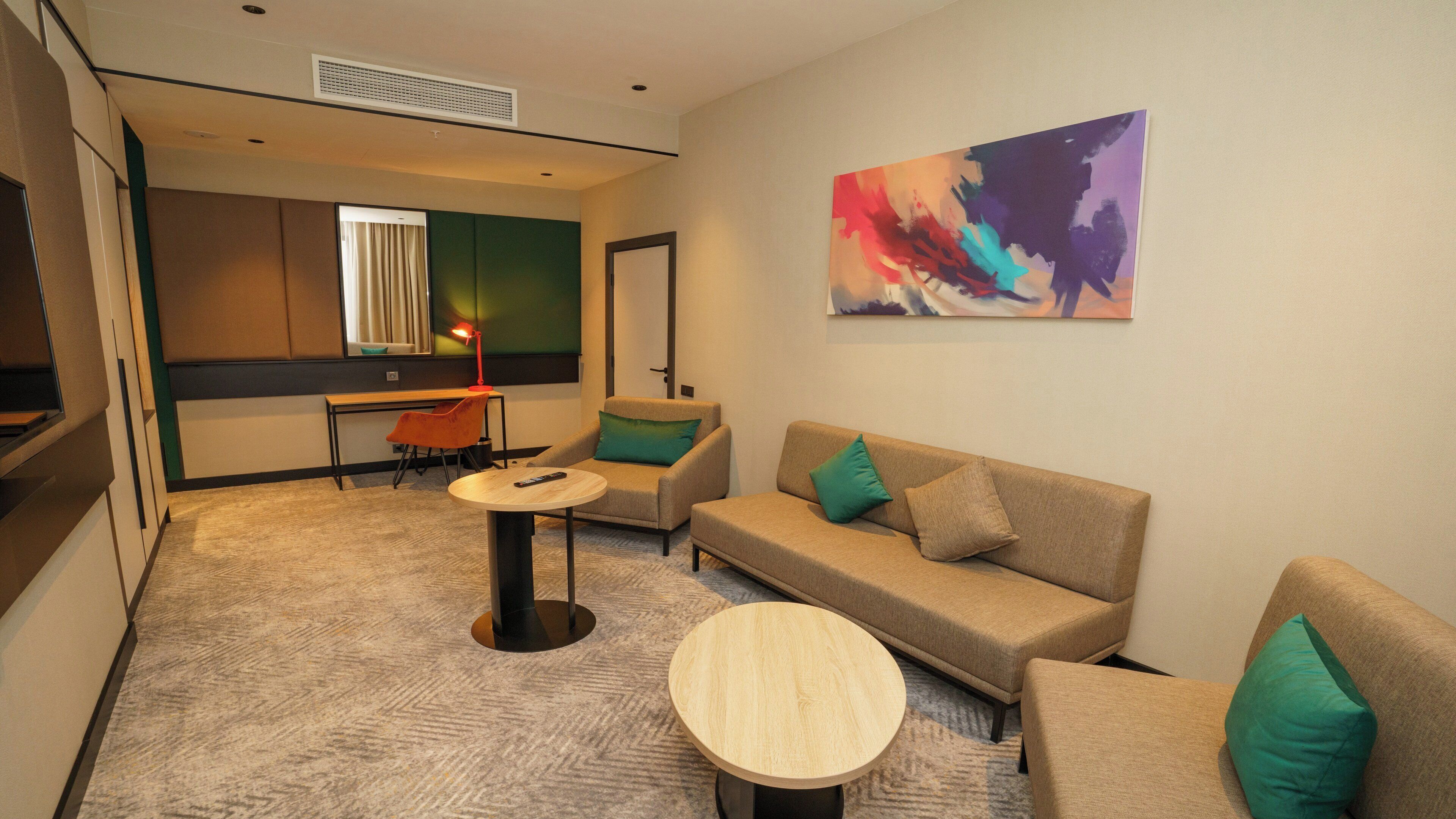 Un salon moderne comprenant un canapé, deux fauteuils, une table basse et un bureau avec une chaise. Un tableau est accroché au mur, et il y a une fenêtre avec des rideaux.