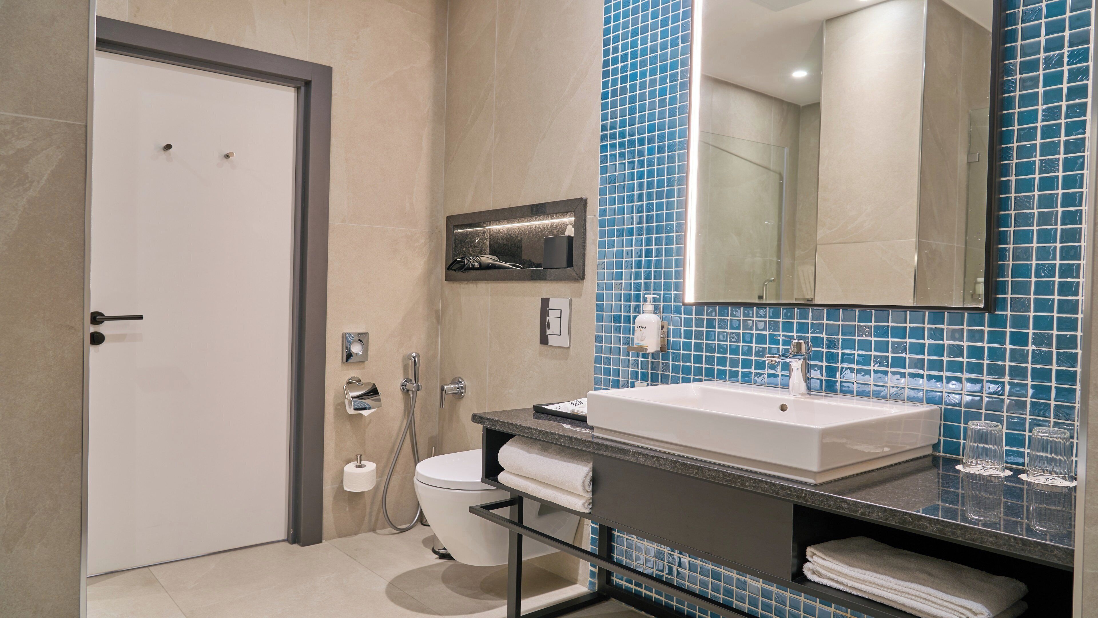 A modern bathroom with a white sink, a glass shower enclosure, and a blue-tiled wall.