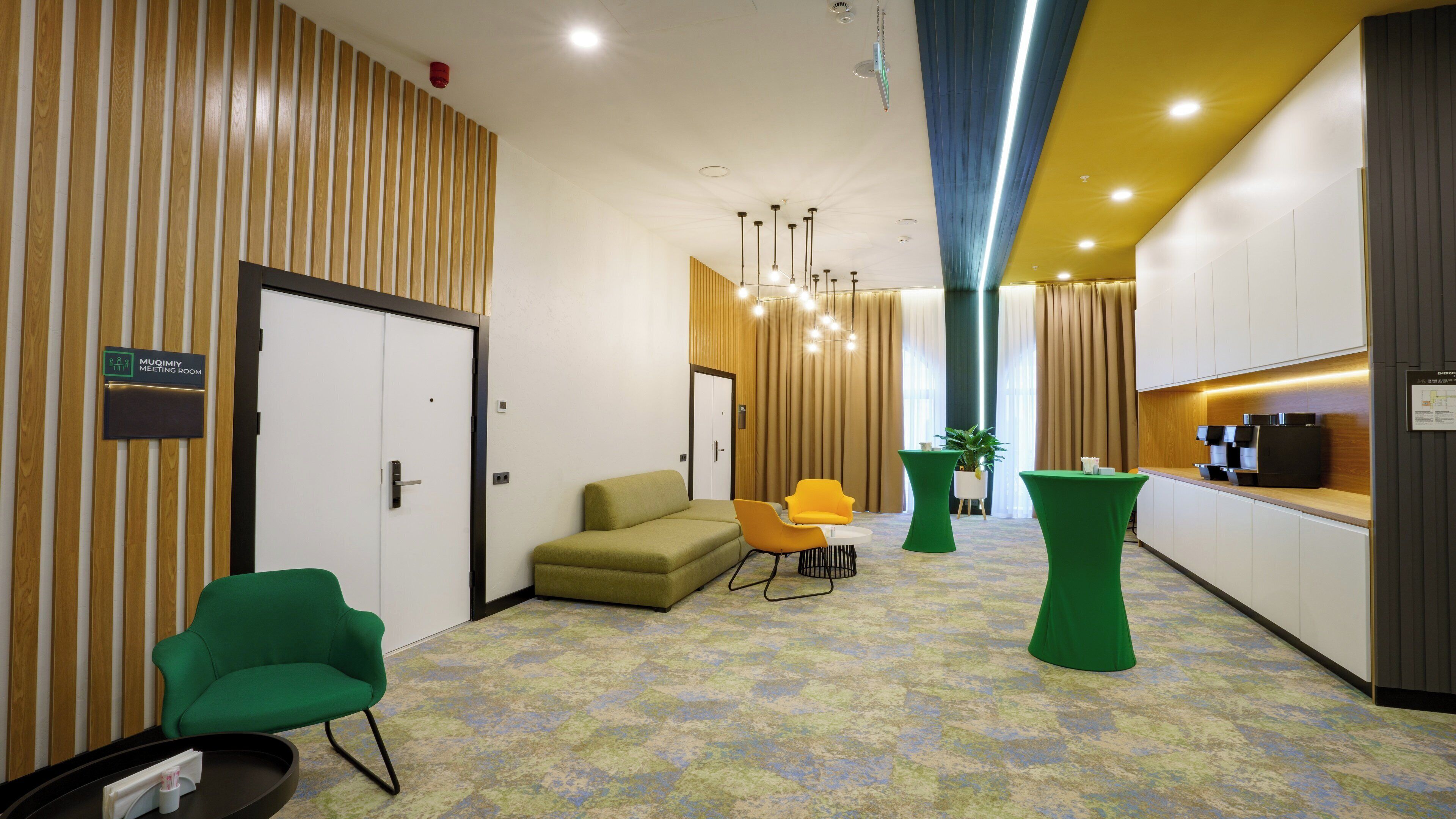 Un hall d’hôtel moderne avec un comptoir d’accueil, un espace salon et un panneau indiquant l’emplacement d’une salle de réunion.