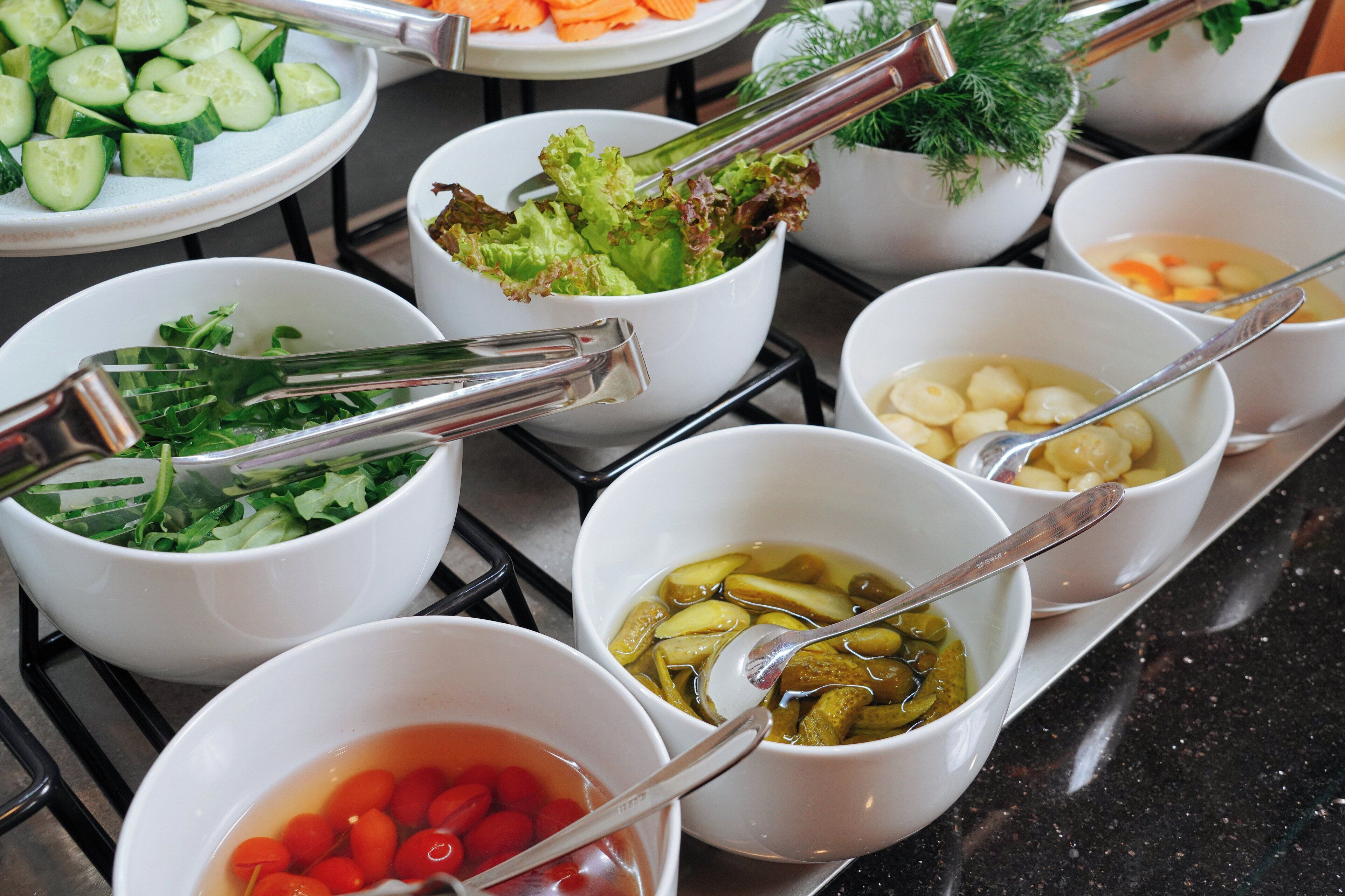 A buffet table with various food items including salads, vegetables, and soups.