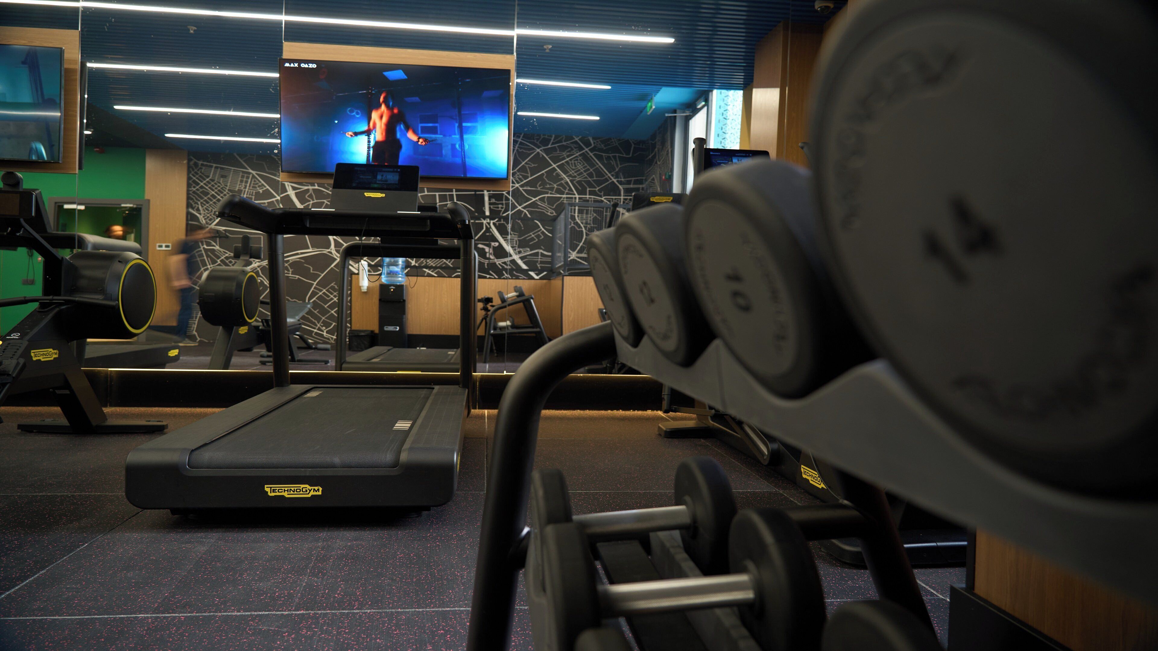 A gym with treadmills, weight machines, and a TV screen displaying a fitness program.