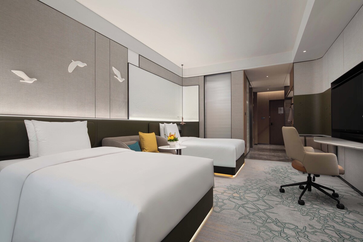 Una habitación de hotel moderna con dos camas, un escritorio, una silla y un televisor.