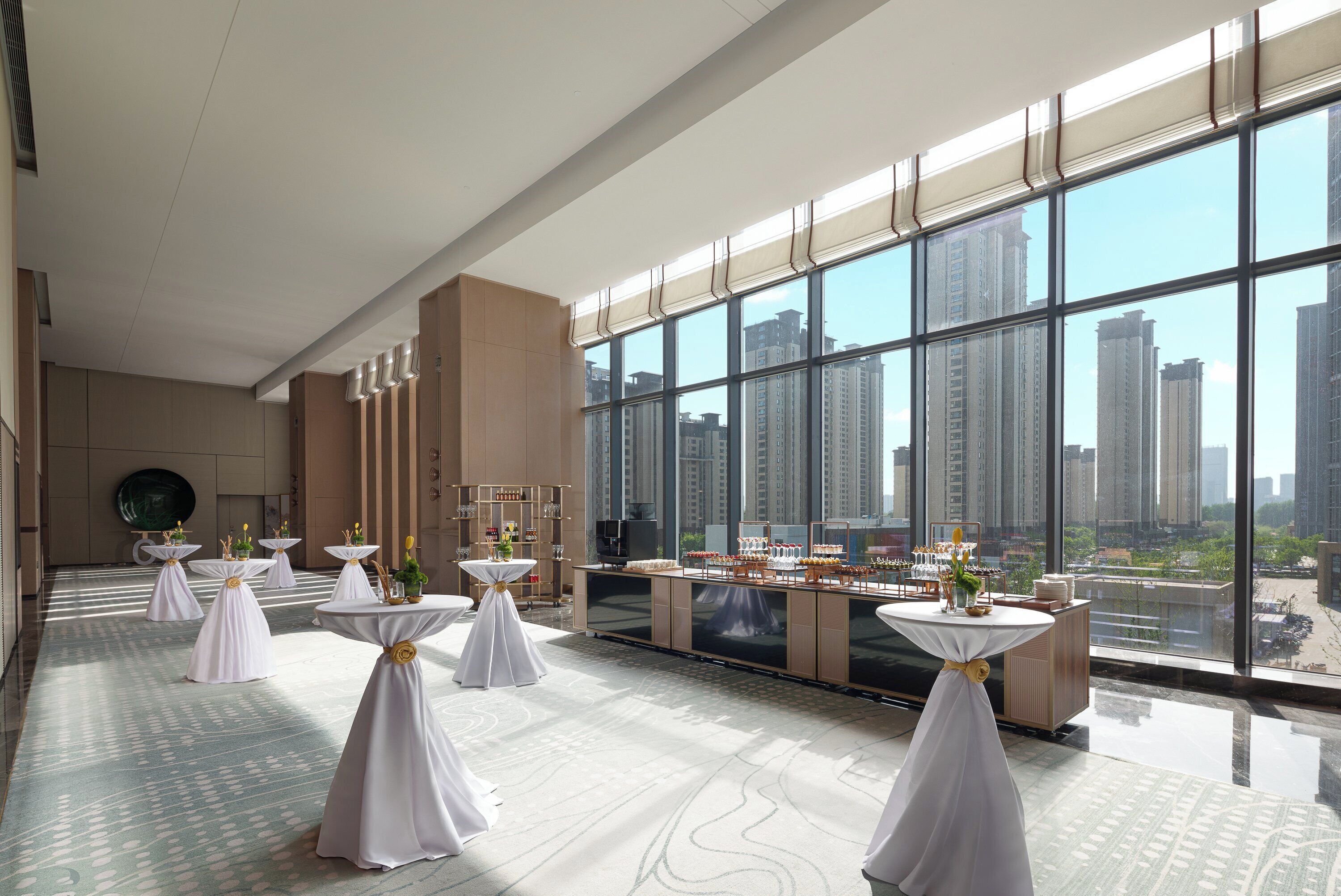 A spacious room with large windows, multiple tables with white tablecloths, and a buffet setup.