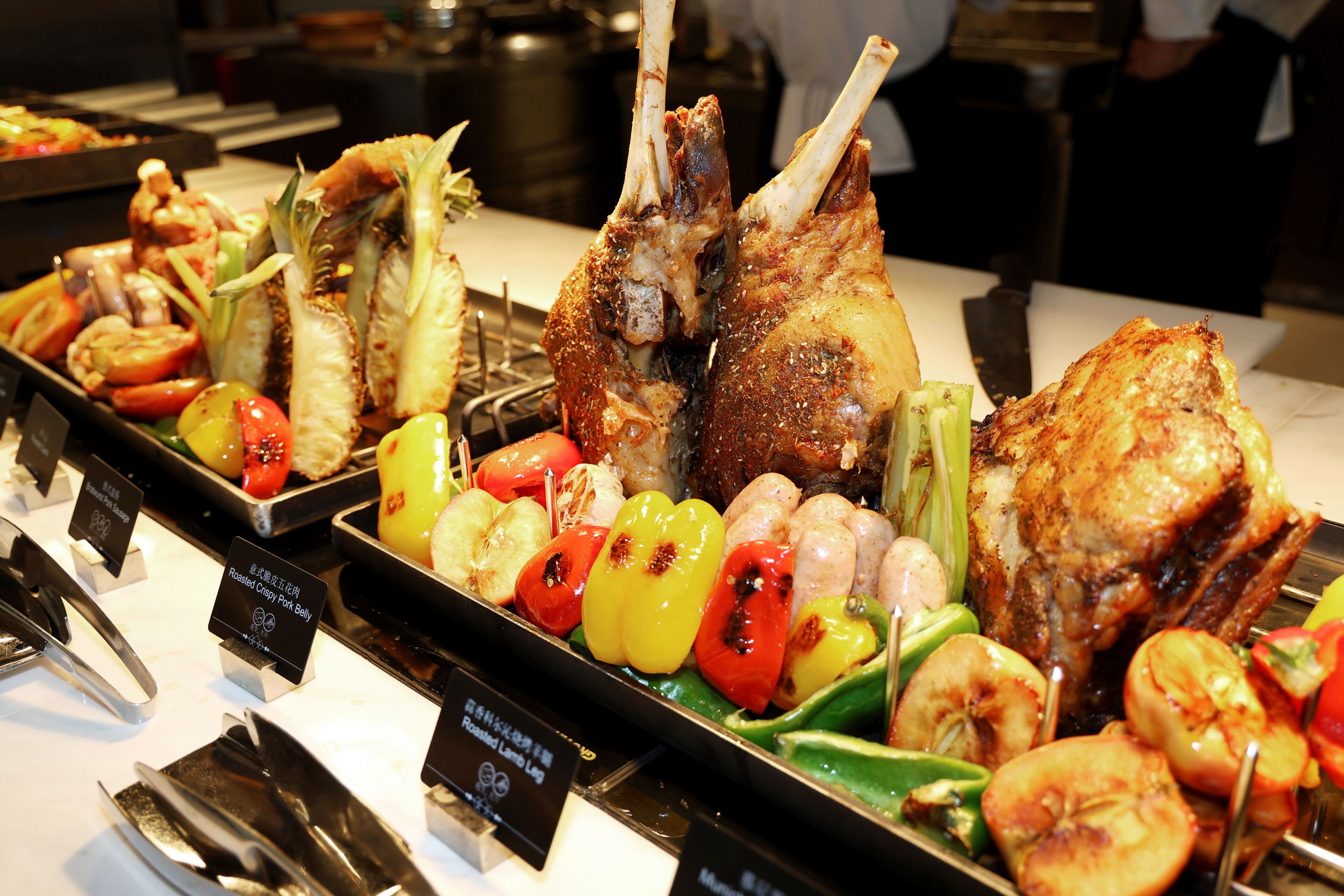 A buffet with roasted meats, vegetables, and skewers.