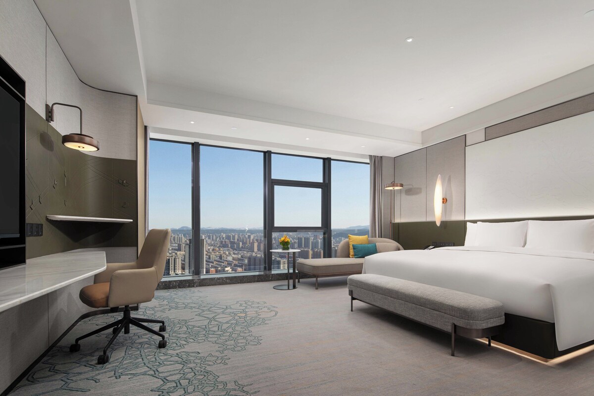 Una habitación de hotel moderna con una cama grande, un escritorio, una silla y vistas a la ciudad.