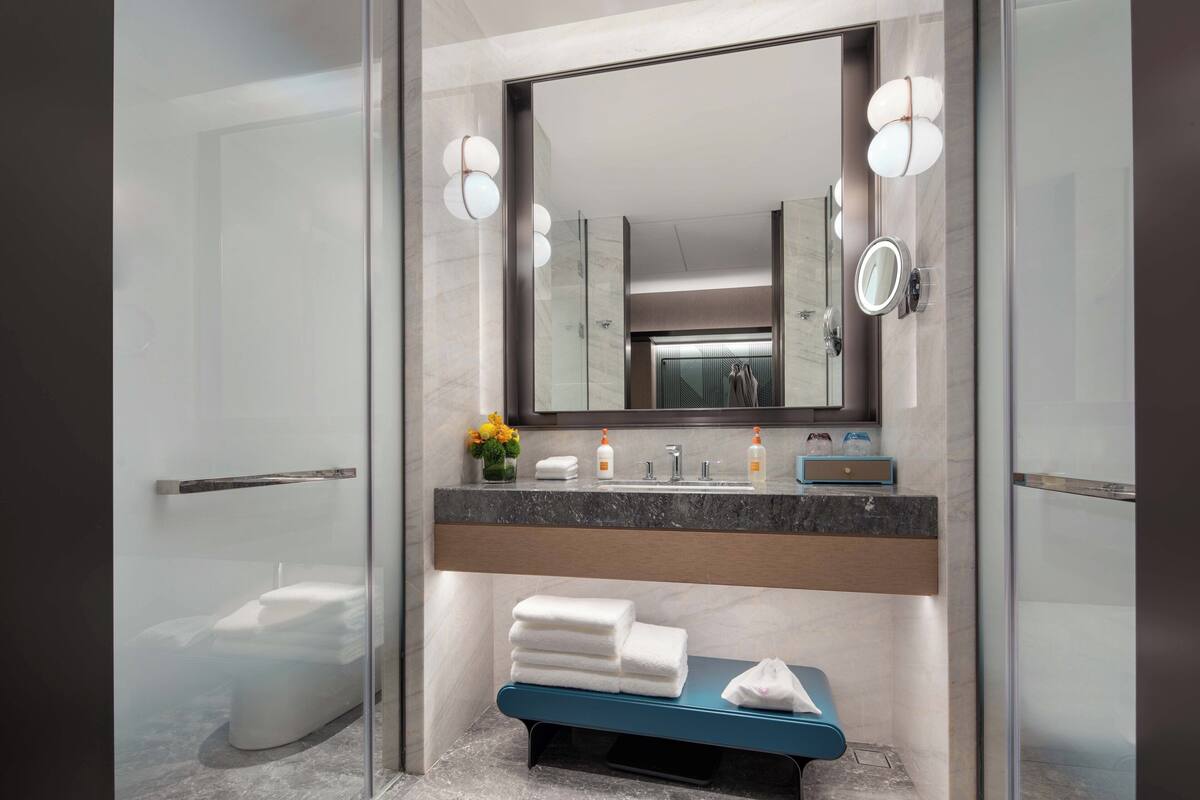 Un baño moderno con cabina de ducha de vidrio, encimera de mármol y un espejo grande con luces empotradas.