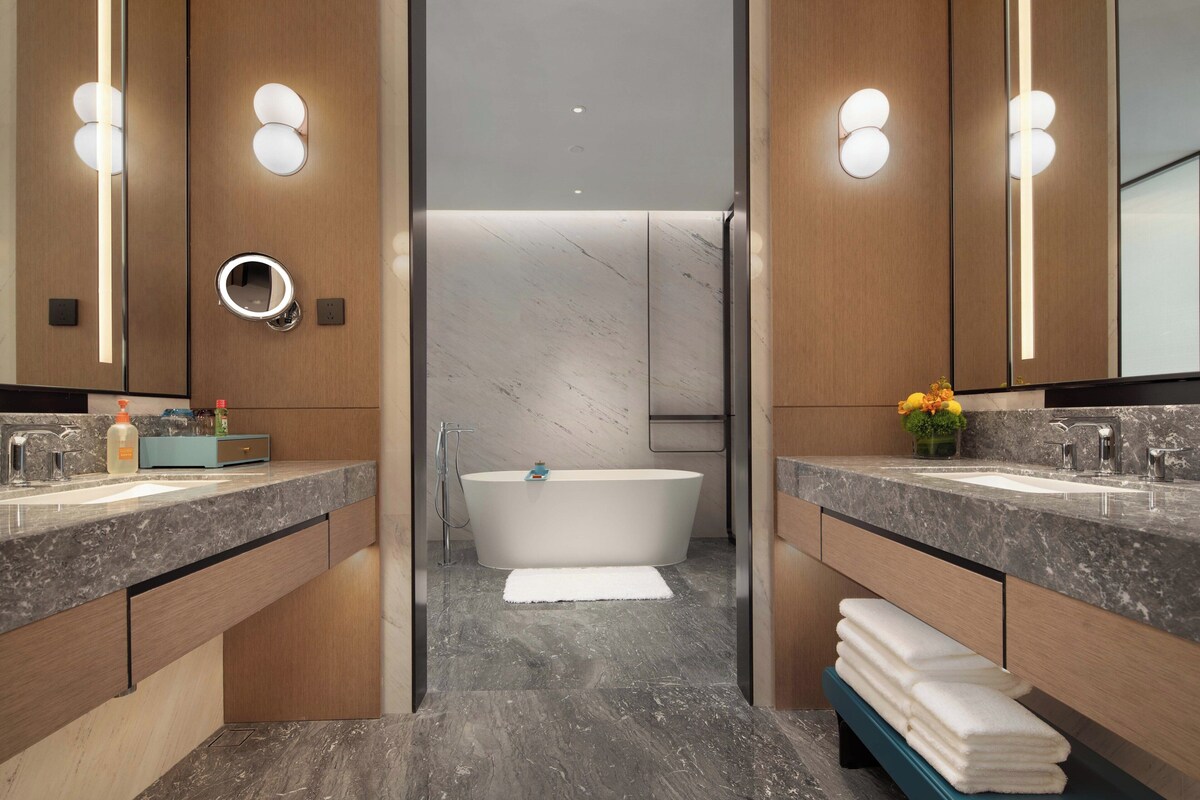 Un baño moderno con una bañera independiente, lavamanos dobles y un espejo de tocador.