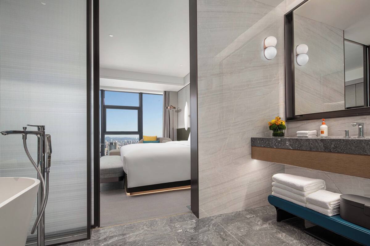 A modern hotel room with a large bed, a bathroom with a bathtub, and a city view.