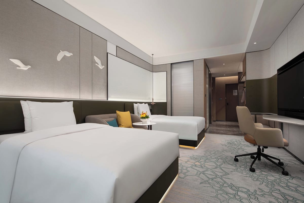 A modern hotel room with two beds, a desk, a chair, and a television.