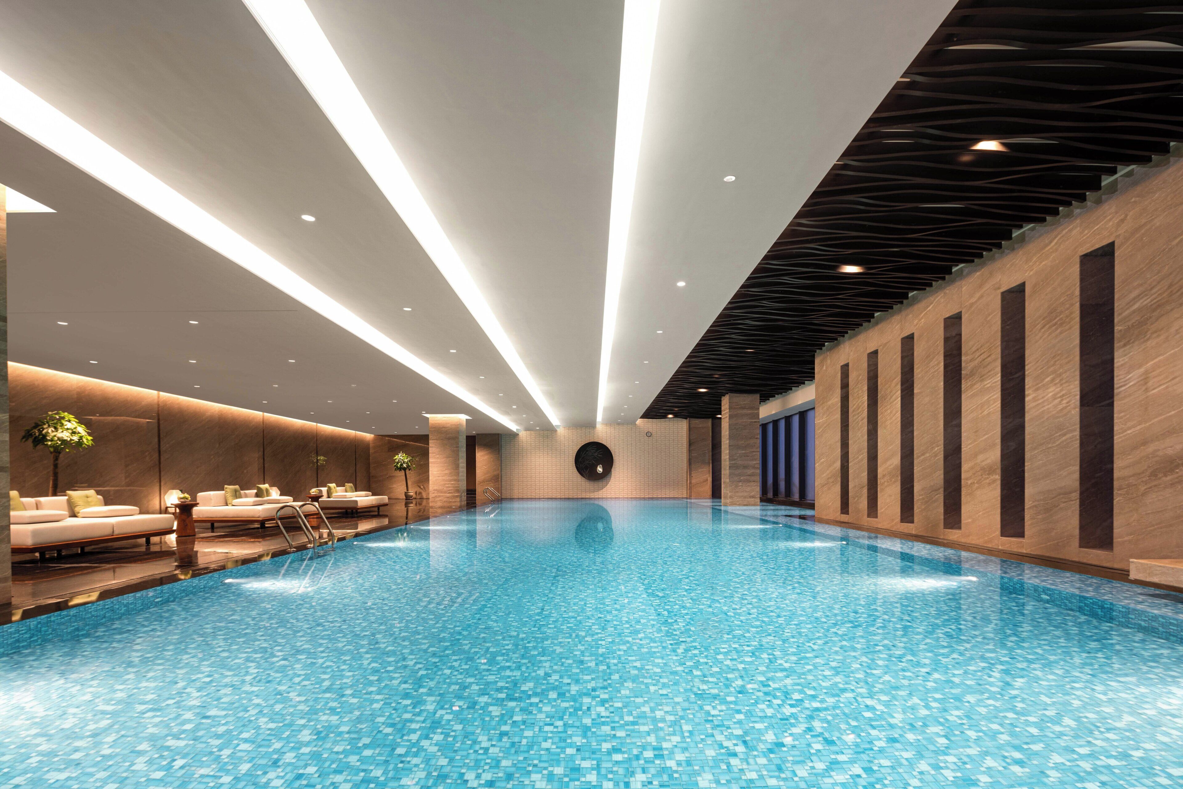 Ein moderner Innenpool mit glasklar blauem Wasser, umgeben von einer Lounge mit Sitzgelegenheiten und einer Holzverkleidung.