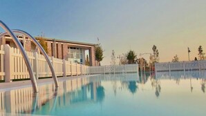 A clear swimming pool with a white fence and a building in the background.