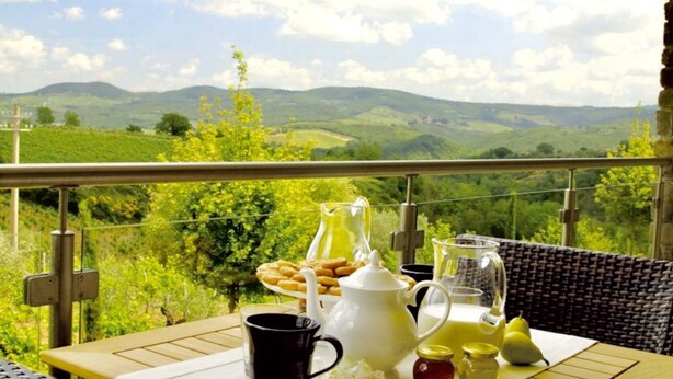 A table set with breakfast items, a pitcher, and a view of green hills.