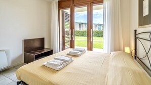 A hotel room with a bed, a desk, and a view of a building and greenery through a sliding door.
