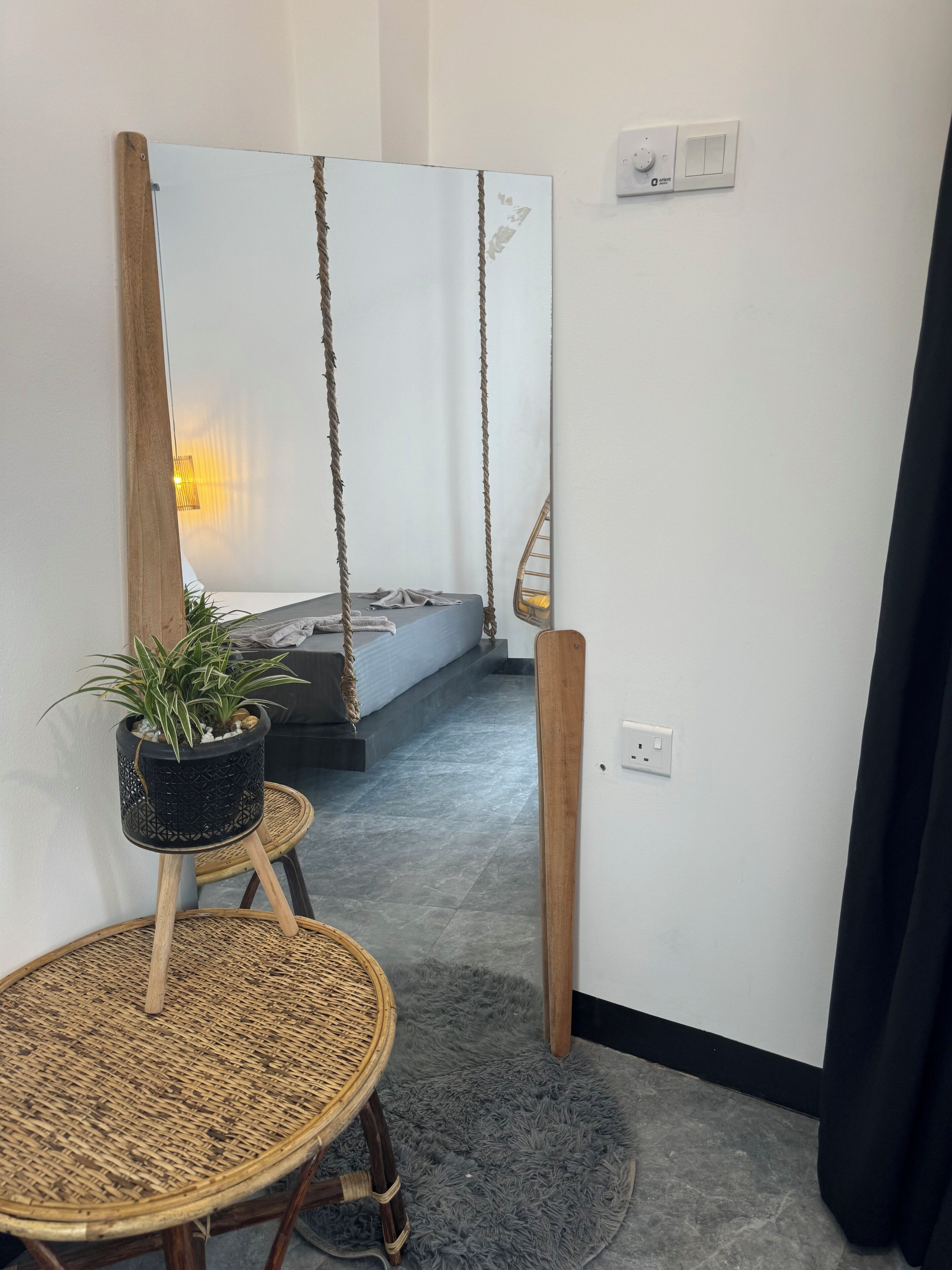 Et værelse med en seng, et lille bord med en plante, en gyngestol og en lampe monteret på væggen.