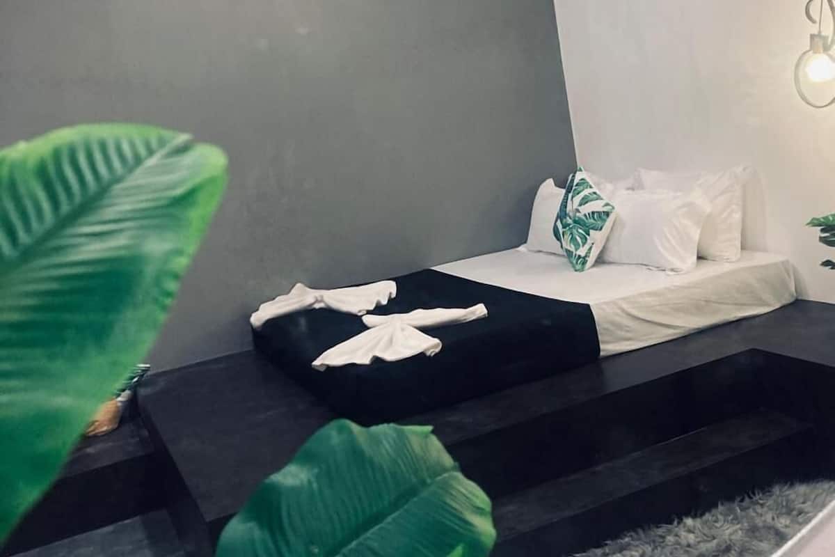 Een moderne slaapkamer met een bed, een klein tafeltje en een plant.