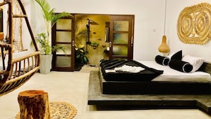 A bedroom with a bed, a ceiling fan, a wall-mounted lamp, a decorative wall piece, and a large window with a view of greenery. - The Jini House - Kabalana (Ahangama)