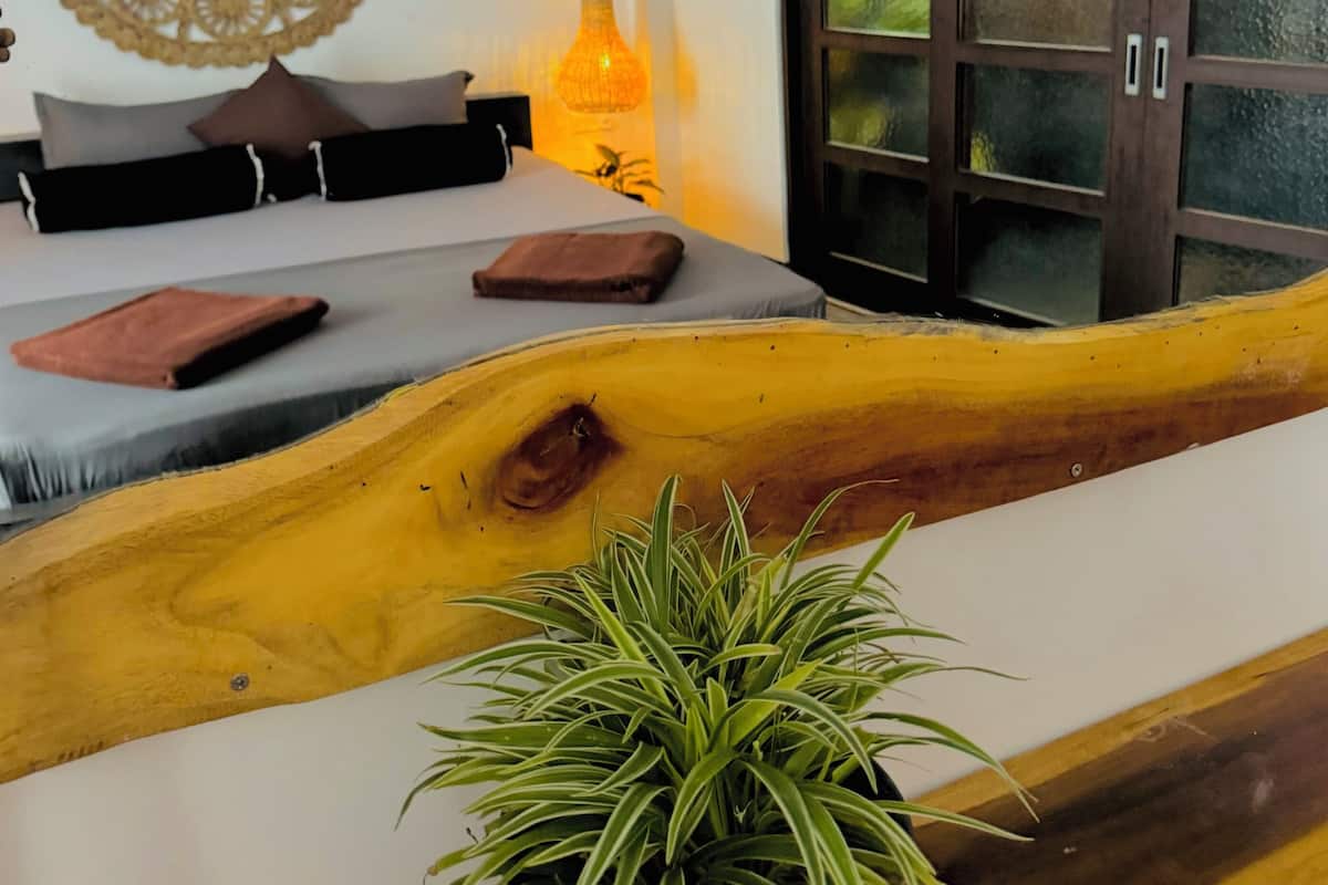 Een slaapkamer met een bed, een potplant, een wanddecoratie en een kast.