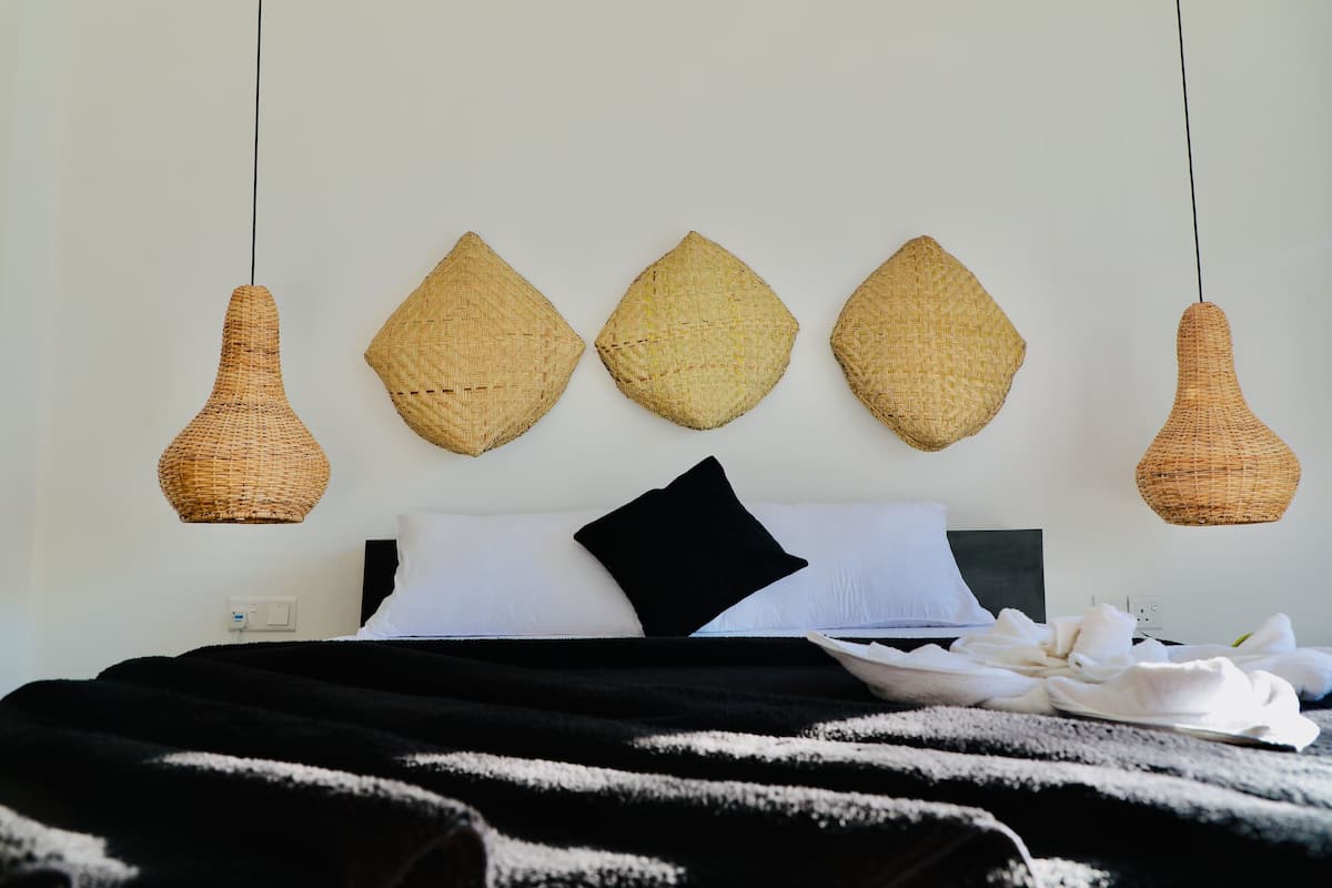 Een bed met een zwart-wit gestreept dekbedovertrek, een wit kussen en een zwart kussen. Daarboven hangen drie geweven wanddecoraties.