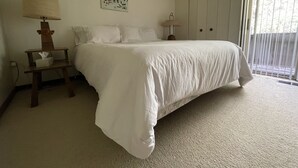 Un dormitorio con una cama grande, una mesita de noche con lámpara, un cuadro en la pared y una ventana con persianas.