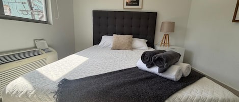 Een slaapkamer met een bed, een bedlampje, een citaat in een lijst op de muur en een raam met uitzicht op elektriciteitskabels.