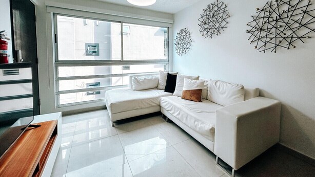 A modern living room with a white sofa, a wooden side table, and a large window. - Bright, Comfy Apt @ Miramar (San Juan)