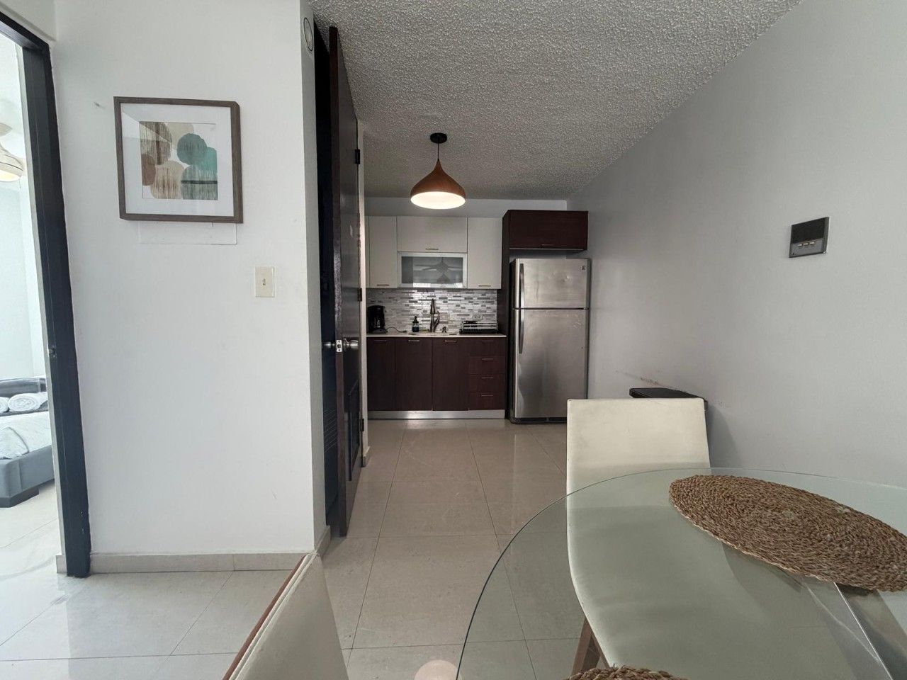 A modern kitchen with stainless steel appliances, a dining area with a glass table, and a hanging pendant light.