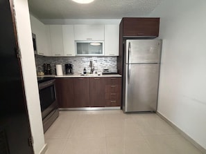 A compact kitchen with white cabinets, a stainless steel refrigerator, and a microwave.