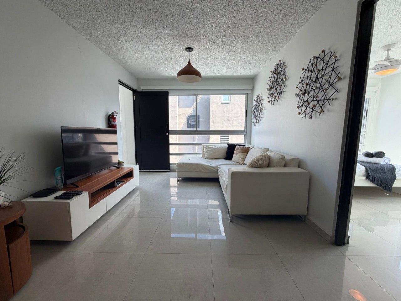A modern living room with a flat-screen TV, a sofa, and a dining area with a wooden table.