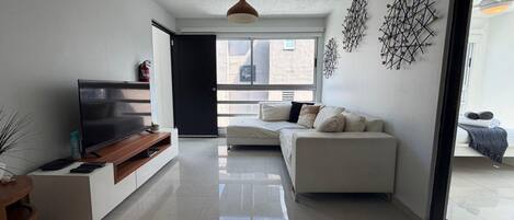 A modern living room with a flat-screen TV, a sofa, and a dining area with a wooden table.