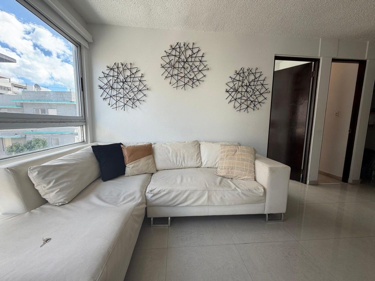 A modern living room with a white sofa, decorative wall art, and a view through a large window.