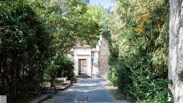 Un sentier pavé de pierres menant à un bâtiment doté d’une porte, le tout entouré de verdure.