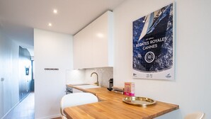Une cuisine moderne avec des armoires blanches, un plan de travail en bois et un évier. Une affiche du Festival de Cannes est accrochée au mur.