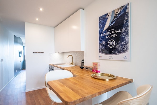 A modern kitchen with white cabinets, a wooden countertop, and a sink. A poster of the Cannes Film Festival is on the wall. - Le Goélette - Superb cosy apartment (Lyon)