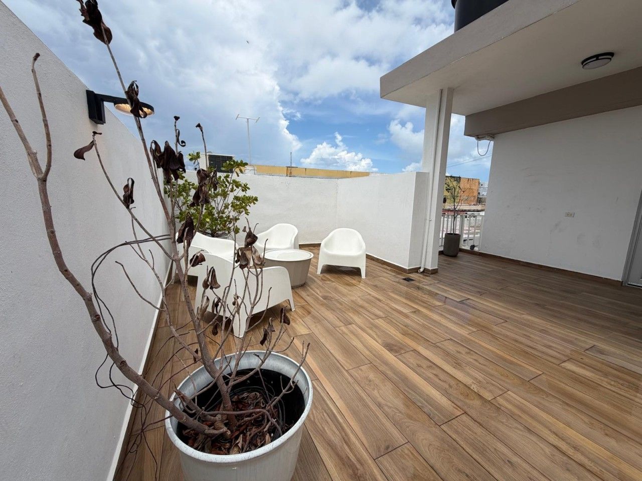 An outdoor patio with a wooden floor, white walls, and a potted plant.
